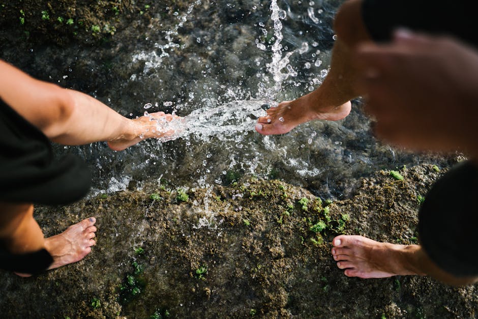 Close-up of bare feet splashing water on rocks outdoors, showcasing playful interaction with nature.