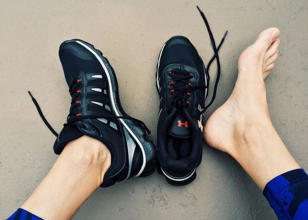 A pair of black sneakers next to bare feet on a gray surface.